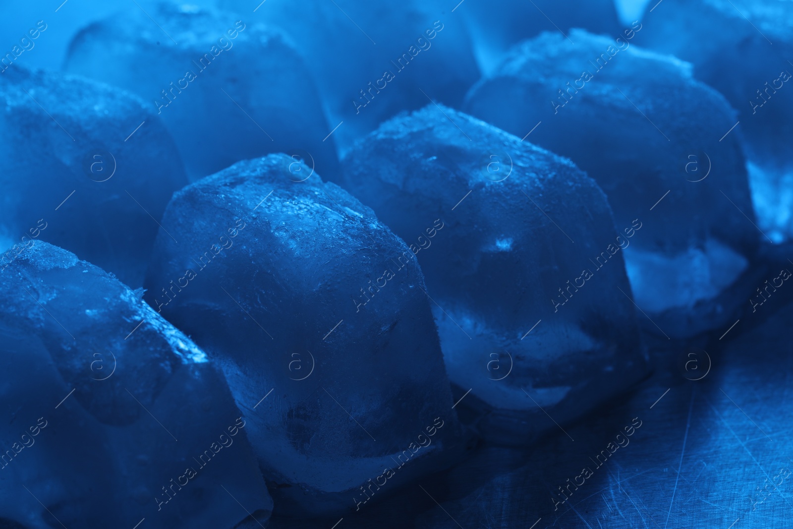 Photo of Crystal clear ice cubes on light blue background, closeup. Color tone effect