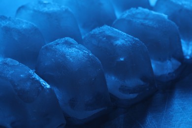 Photo of Crystal clear ice cubes on light blue background, closeup. Color tone effect