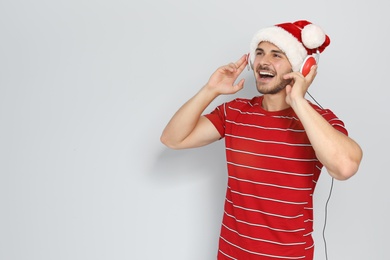 Photo of Young man in Santa hat listening to Christmas music on color background