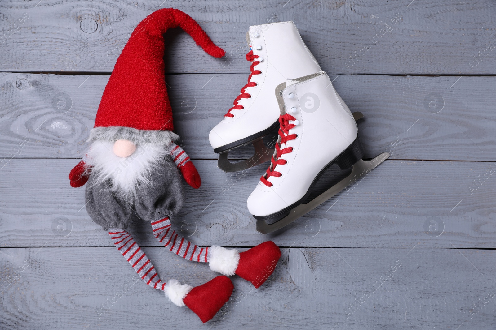 Photo of Pair of ice skates with Christmas gnome on grey wooden background, flat lay