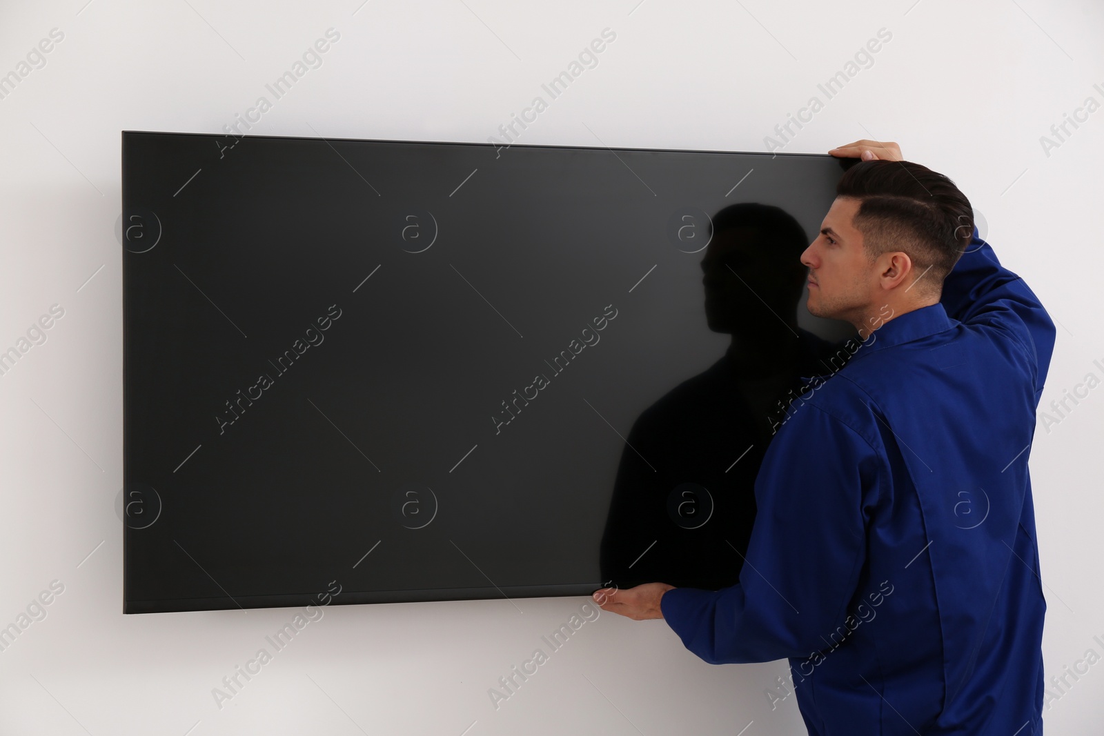 Photo of Professional technician installing modern flat screen TV on wall indoors