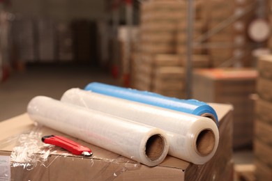 Photo of Rolls of different stretch wraps and utility knife on boxes in warehouse