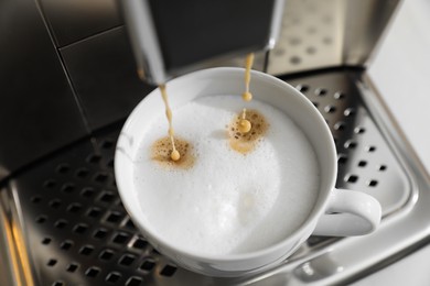 Photo of Modern coffee machine making cappuccino into cup, closeup
