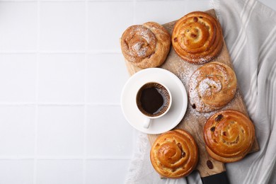 Photo of Sweet buns. Delicious rolls with raisins, powdered sugar and coffee cup on white tiled table, top view. Space for text