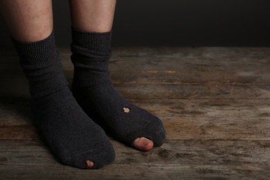 Photo of Poor person in shabby socks on wooden floor, closeup