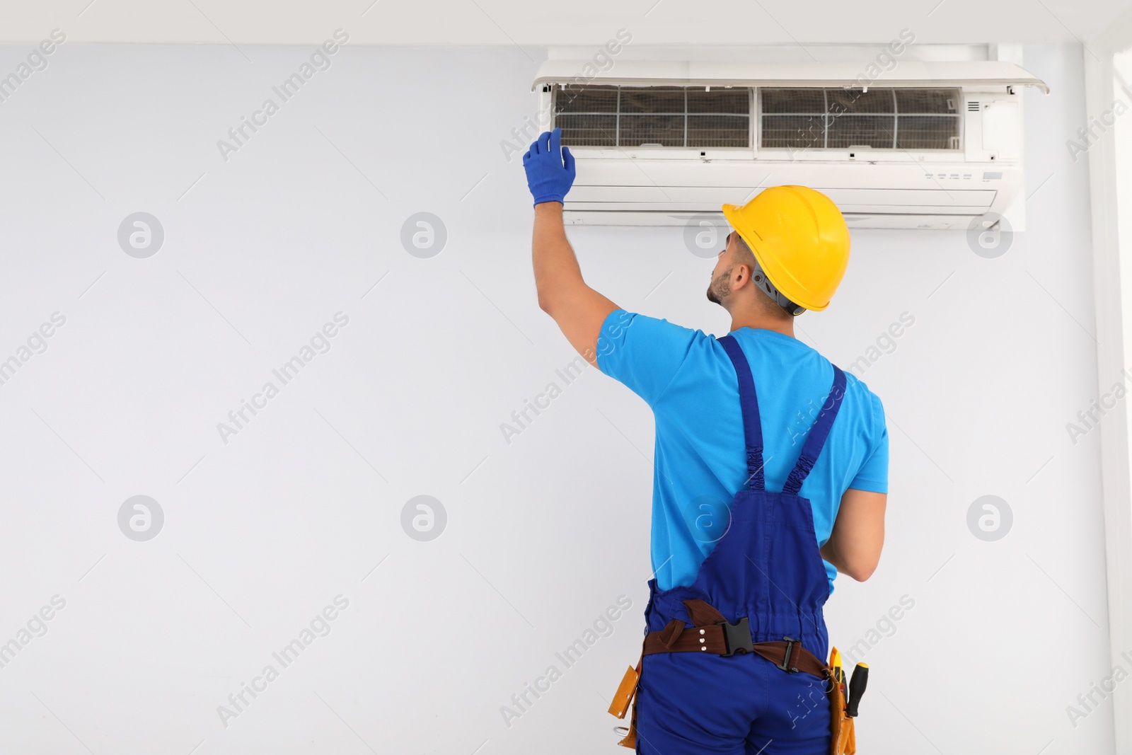 Photo of Professional technician maintaining modern air conditioner indoors. Space for text