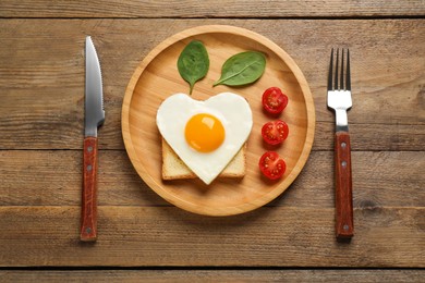 Photo of Tasty fried egg in shape of heart with toast served on wooden table, flat lay