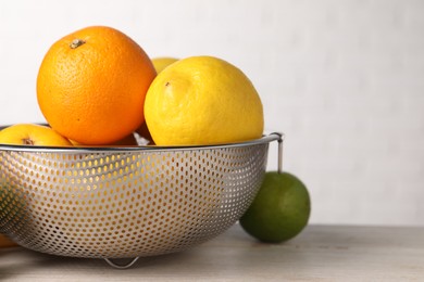 Different fresh fruits in colander on white wooden table, closeup. Space for text