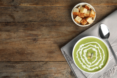 Photo of Delicious broccoli cream soup served on wooden table, flat lay. Space for text