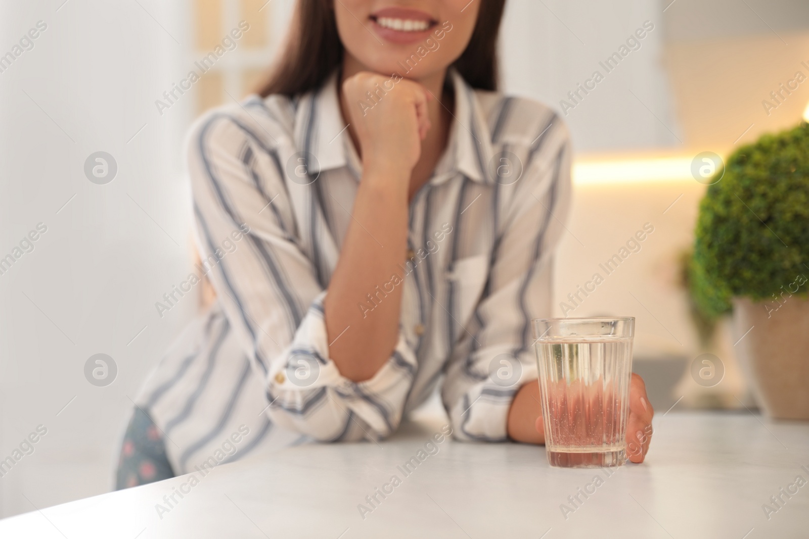 Photo of Young woman with glass of pure water at countertop in kitchen, closeup