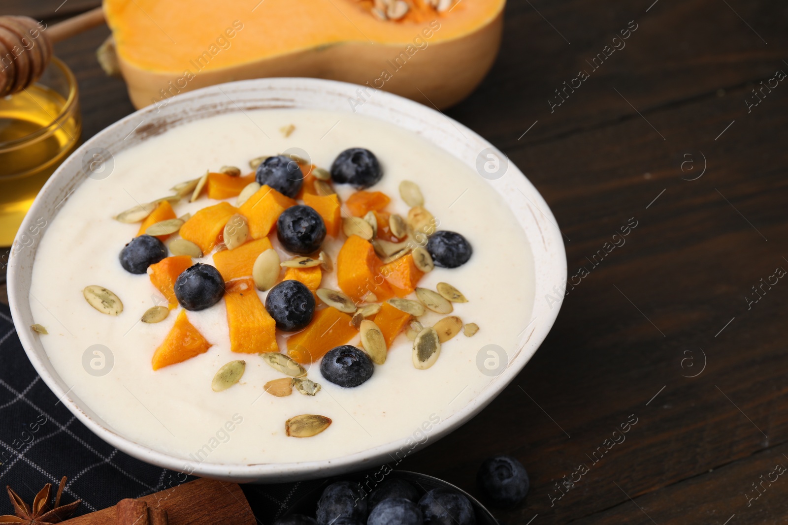 Photo of Bowl of delicious semolina pudding with blueberries, pumpkin and seeds on table, closeup