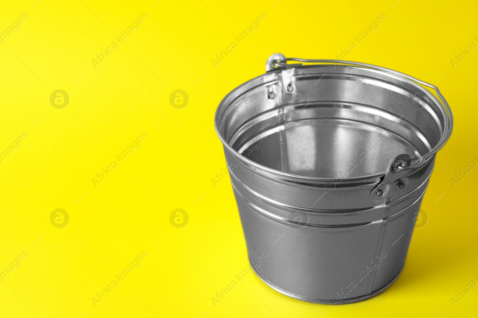 Photo of One shiny metal bucket on yellow background. Space for text