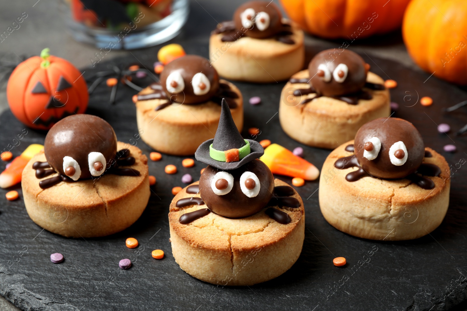 Photo of Delicious biscuits with chocolate spiders on slate plate, closeup. Halloween celebration