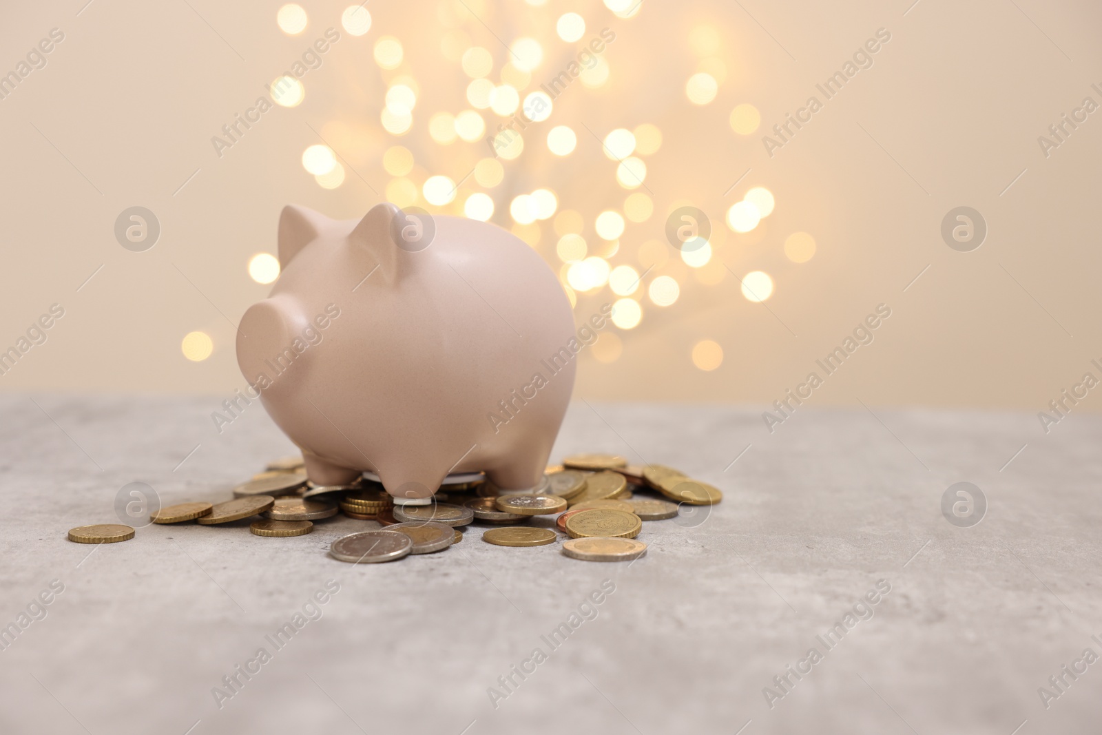 Photo of Piggy bank and coins on grey table against blurred lights, space for text