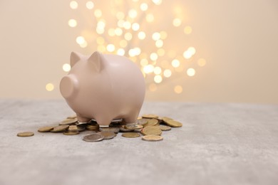 Photo of Piggy bank and coins on grey table against blurred lights, space for text