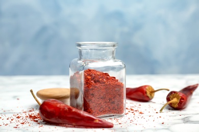 Jar with crushed chili pepper and pods on table