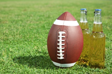 Photo of Ball for American football and beverage on fresh green field grass. Space for text