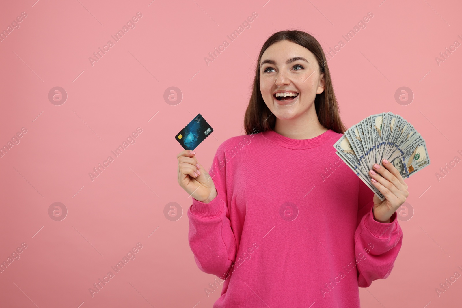 Photo of Happy woman with credit card and dollar banknotes on pink background, space for text