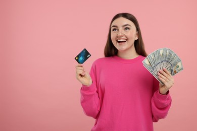 Photo of Happy woman with credit card and dollar banknotes on pink background, space for text