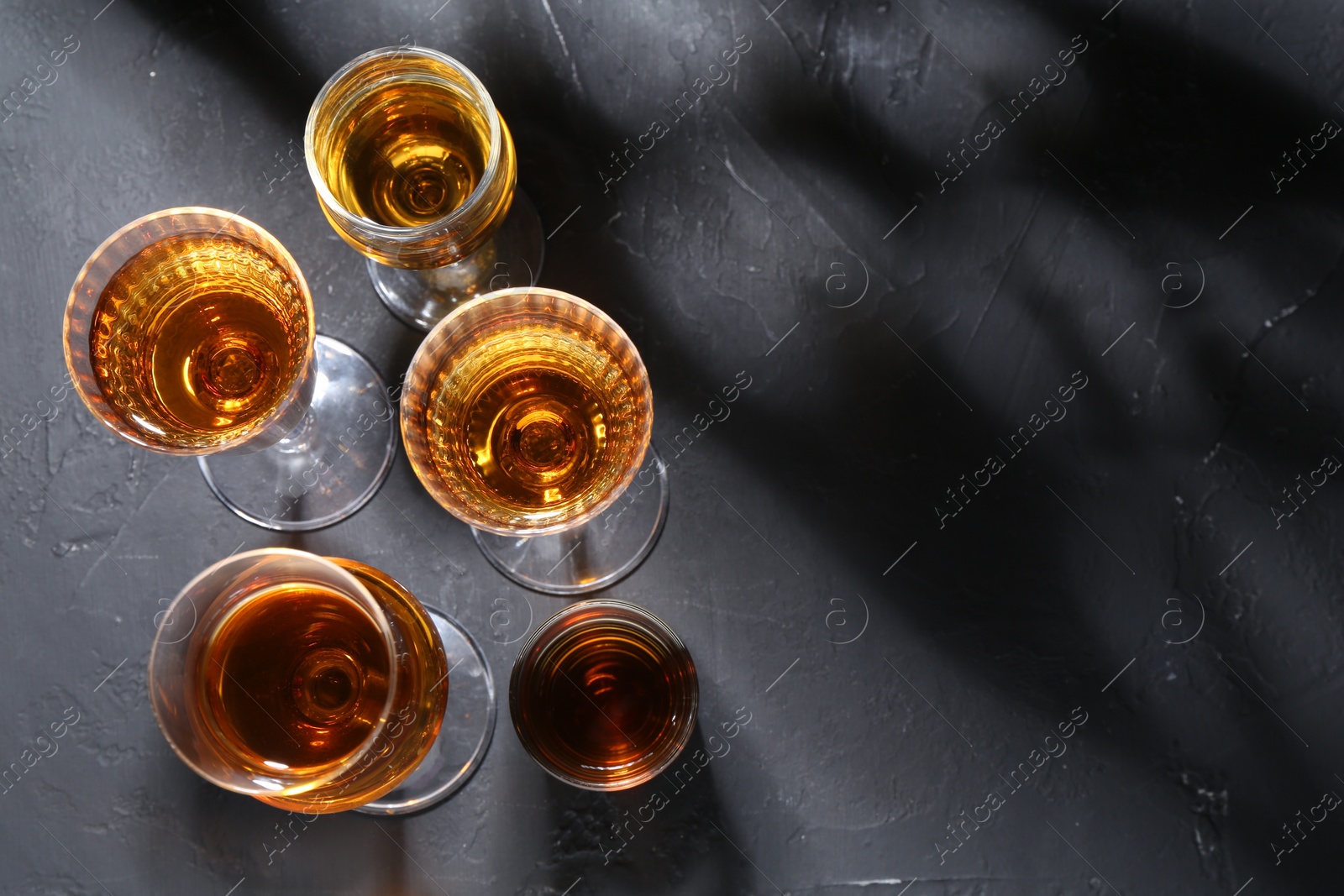 Photo of Many different liqueurs in glasses on dark textured table, flat lay. Space for text