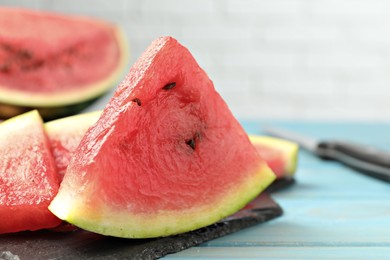 Photo of Slate board with slices of juicy watermelon on light blue wooden table, closeup