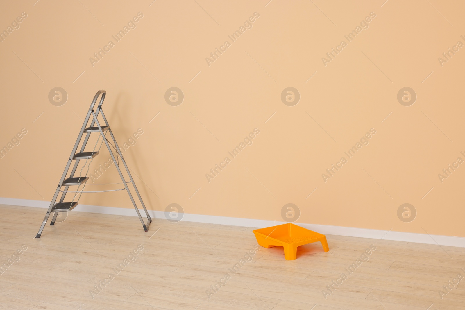 Photo of Metal stepladder near pale orange wall indoors, space for text. Room renovation