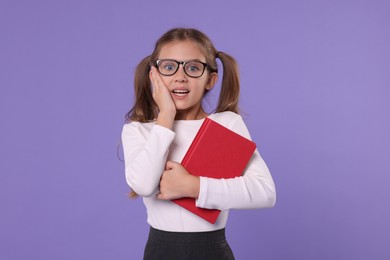 Photo of Excited schoolgirl with book on violet background