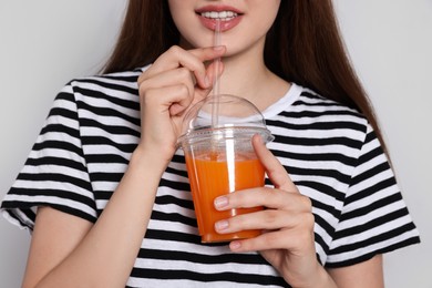 Young woman drinking juice from plastic cup on light grey background, closeup