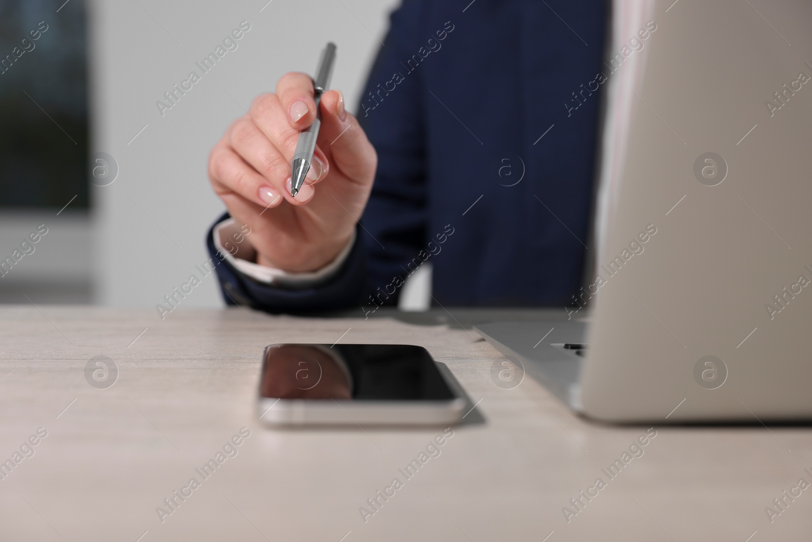 Photo of Woman with smartphone and pen working on laptop at wooden table, closeup. Electronic document management