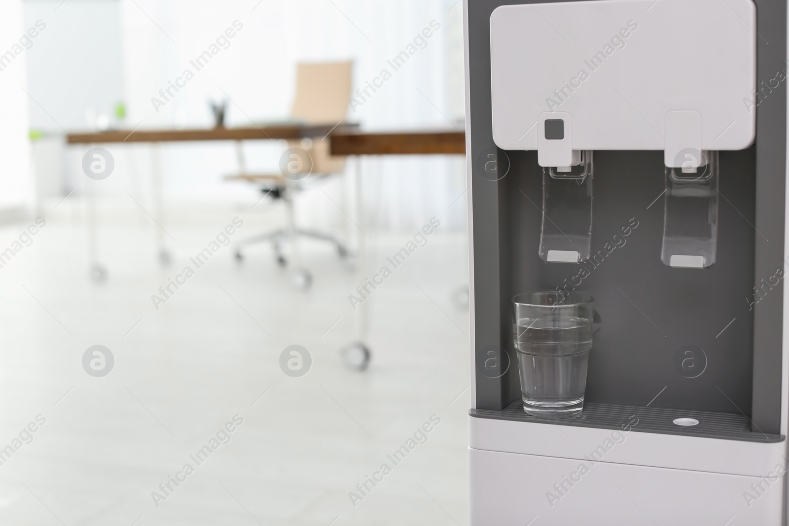 Photo of Modern water cooler with glass in office, closeup. Space for text