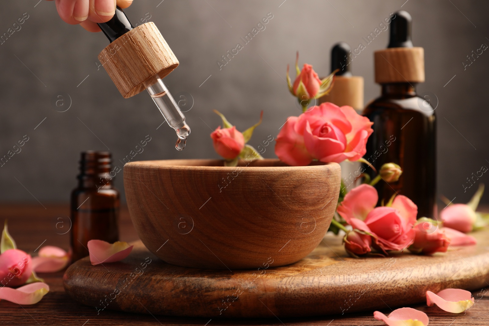 Photo of Woman dripping essential oil into bowl at wooden table, closeup. Aromatherapy treatment