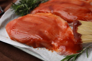 Photo of Raw marinated meat, rosemary and basting brush on table, closeup
