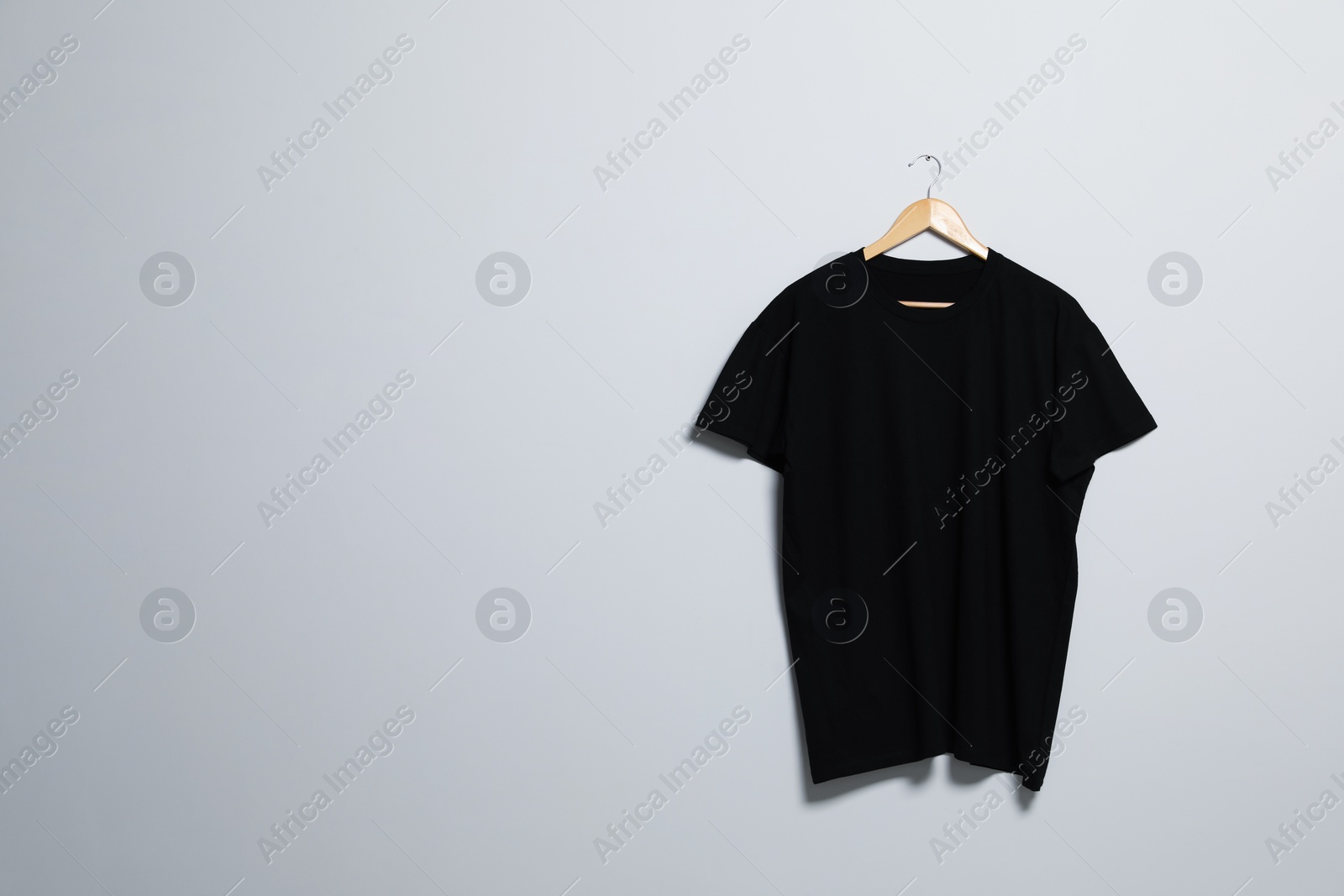 Photo of Hanger with black t-shirt on light wall. Mockup for design