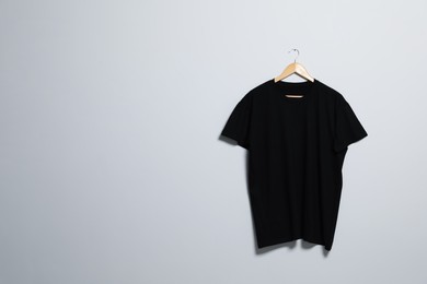 Photo of Hanger with black t-shirt on light wall. Mockup for design