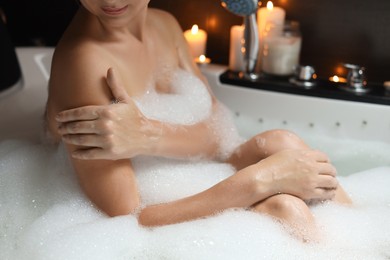 Photo of Woman taking bubble bath indoors, closeup. Romantic atmosphere