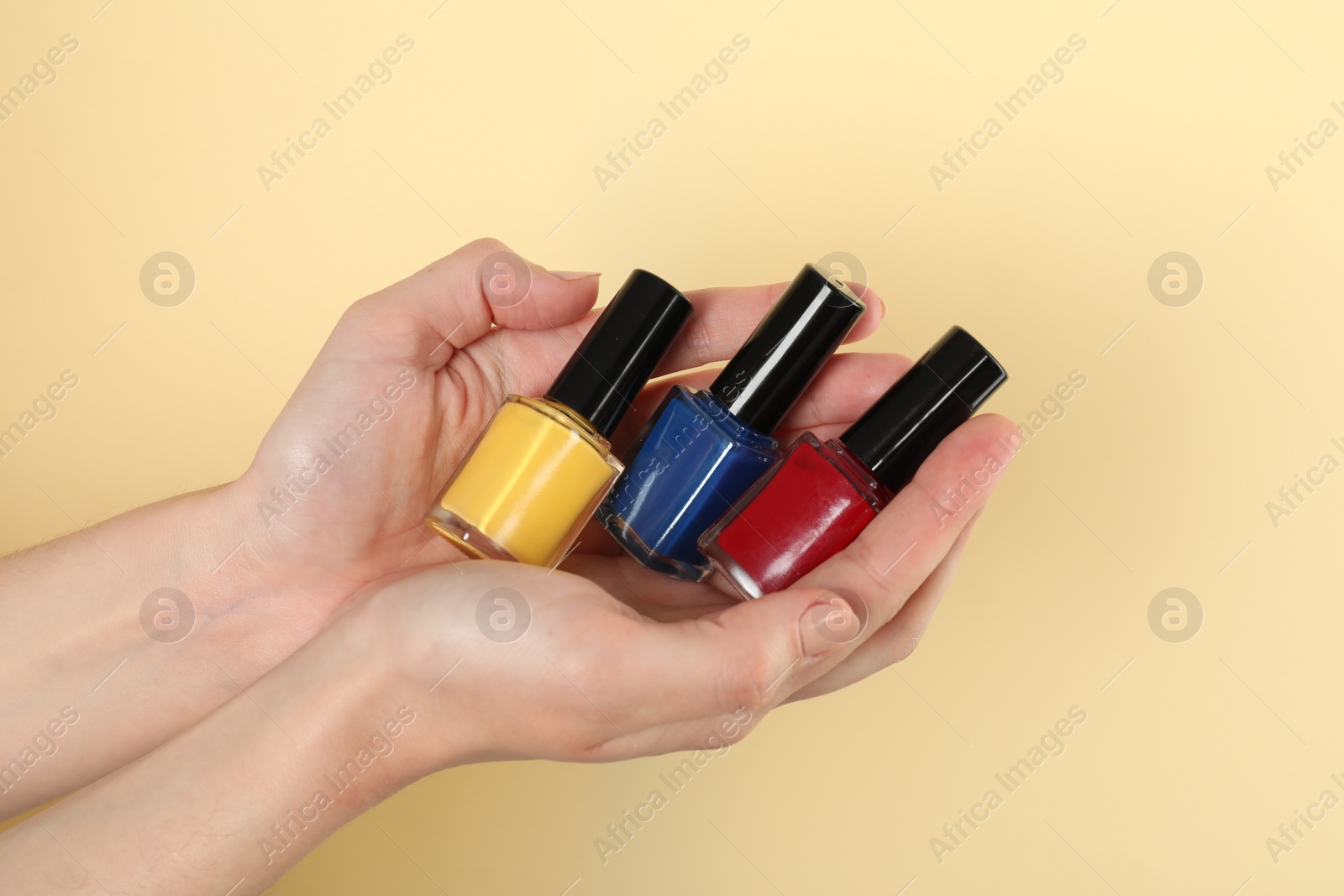 Photo of Woman holding nail polishes on beige background, closeup