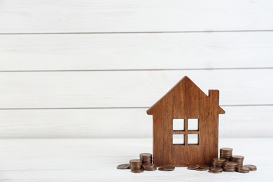 Photo of House model and coins on white wooden table. Space for text