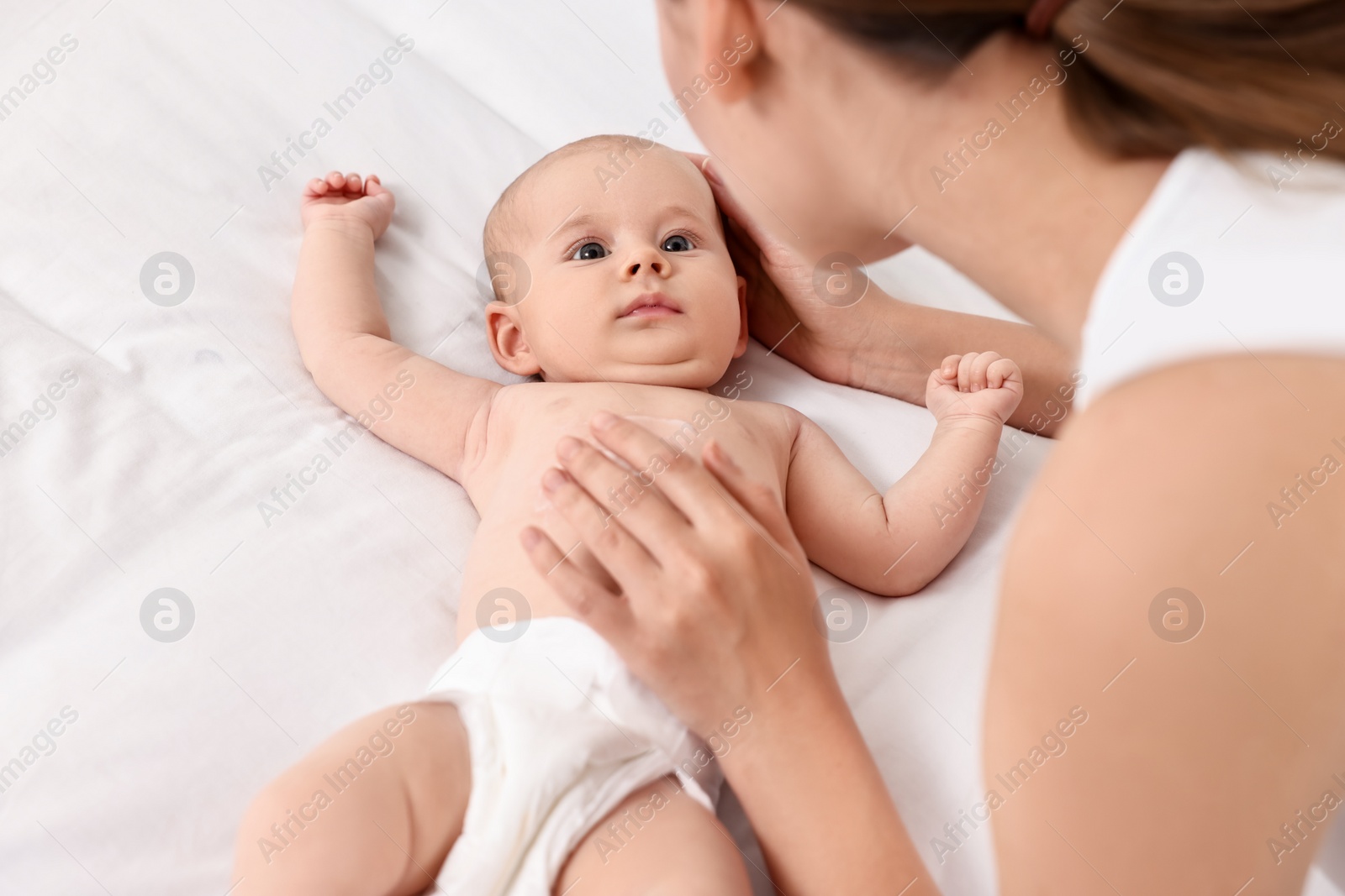 Photo of Woman applying body cream onto baby`s skin on bed, closeup