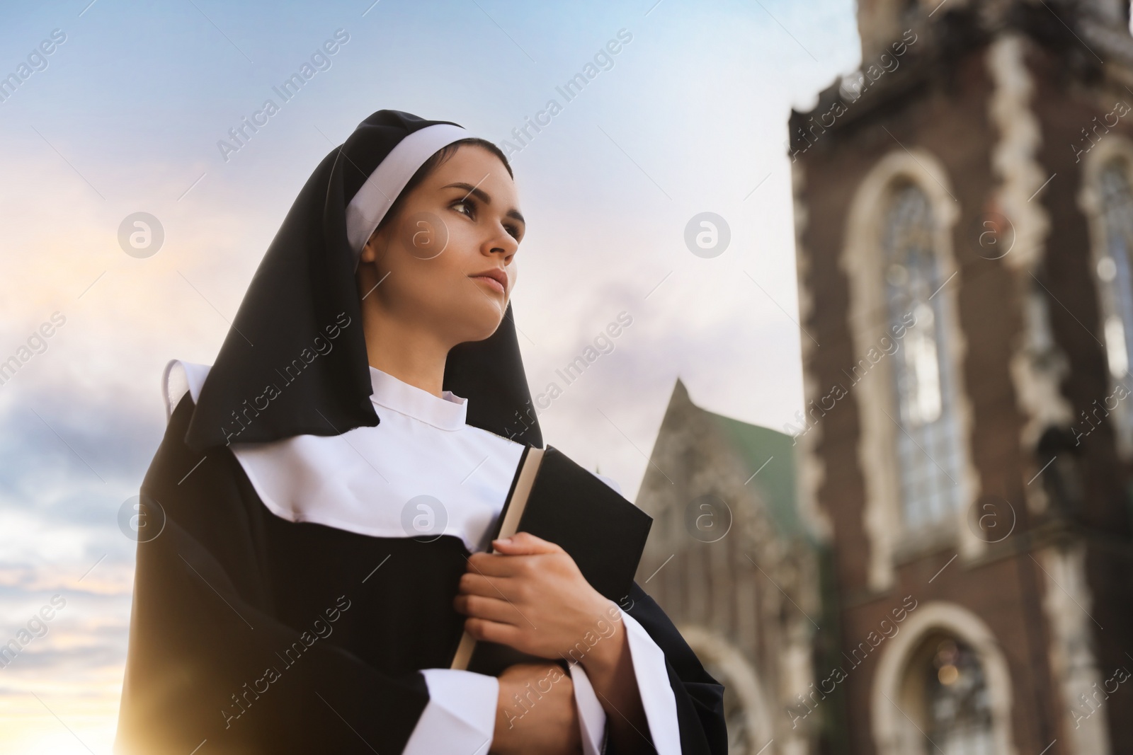 Photo of Young nun with Bible near cathedral outdoors on sunny day, space for text