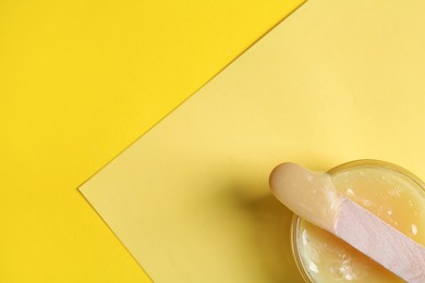 Photo of Spatula with wax on yellow background, top view. Space for text