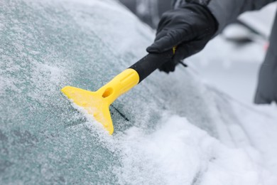 Photo of Man cleaning snow from car windshield outdoors, closeup