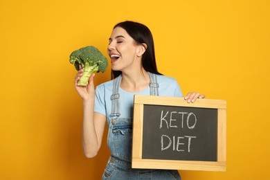 Photo of Happy woman holding broccoli and chalkboard with words Keto Diet on yellow background