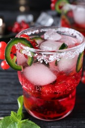 Photo of Spicy red currant cocktail with jalapeno on black wooden table, closeup