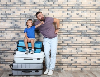 Man and his son with suitcases near brick wall. Space for text