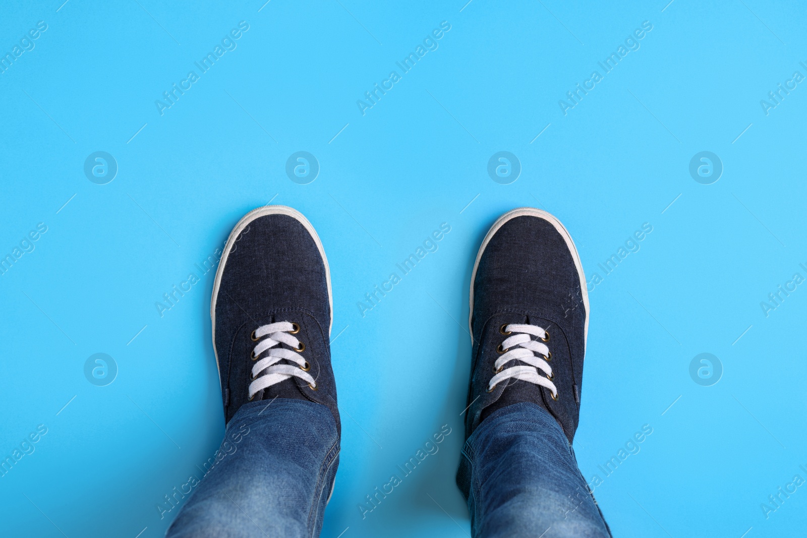 Photo of Child in stylish sneakers standing on light blue background, top view
