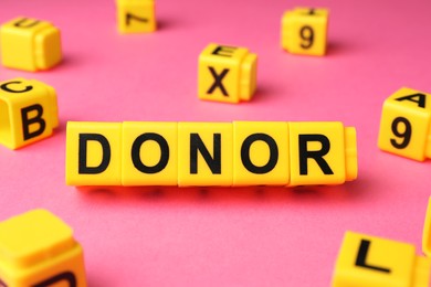 Photo of Word Donor made of yellow cubes on pink background, closeup