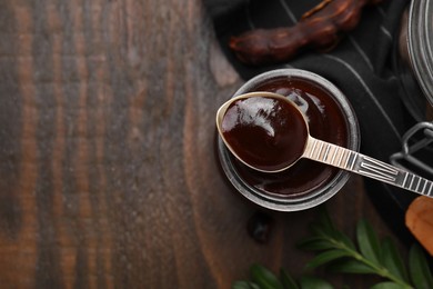 Photo of Jar of tasty tamarind sauce, spoon and fresh pods on wooden table, flat lay. Space for text