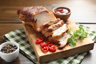 Photo of Pieces of baked pork belly served with sauce, chili pepper and parsley on wooden table, closeup