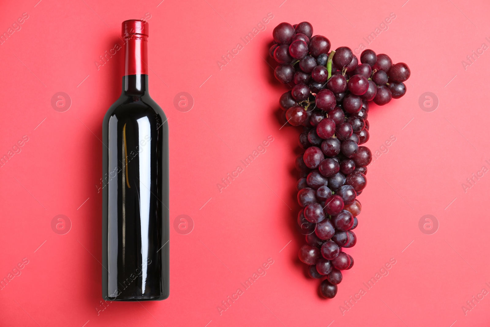 Photo of Fresh ripe juicy grapes and bottle of wine on red background, flat lay