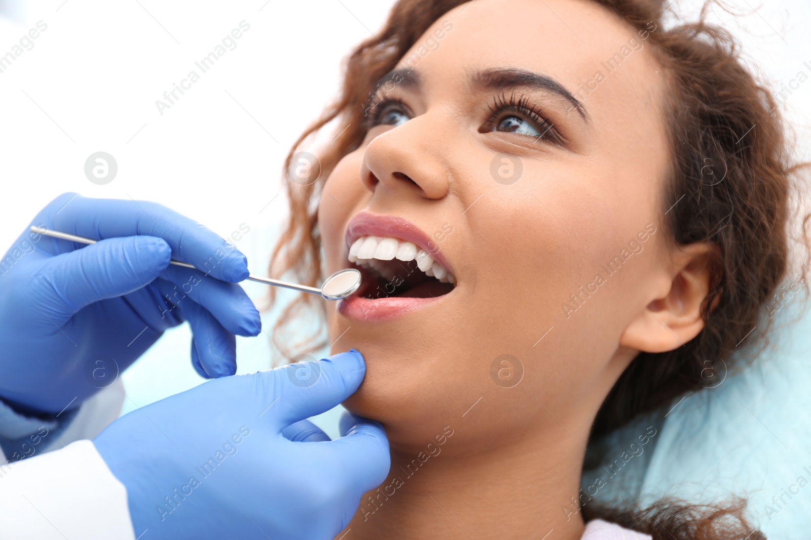 Photo of Dentist examining African-American woman's teeth with mirror in hospital